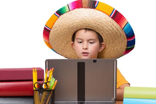 Young boy in his Meican hat studying on his laptop betwwen the books