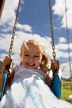 Litte toddler girl on the swing having great time, holding the chaing strongly