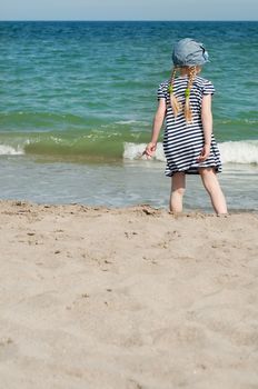 Small girl in hat and dress on sand beach