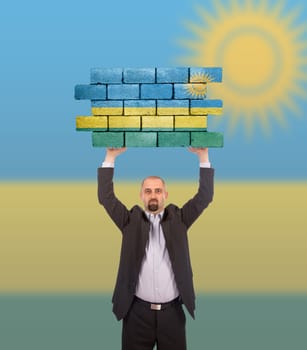 Businessman holding a large piece of a brick wall, flag of Rwanda, isolated on national flag