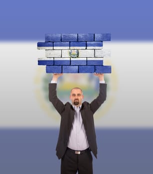 Businessman holding a large piece of a brick wall, flag of El Salvador, isolated on national flag