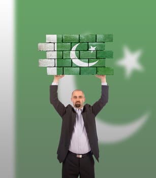 Businessman holding a large piece of a brick wall, flag of Pakistan, isolated on national flag