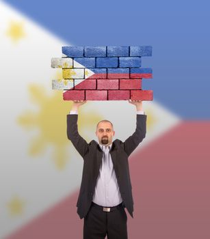 Businessman holding a large piece of a brick wall, flag of the Philippines, isolated on national flag