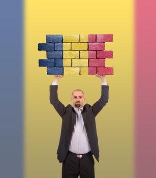 Businessman holding a large piece of a brick wall, flag of Romania, isolated on national flag