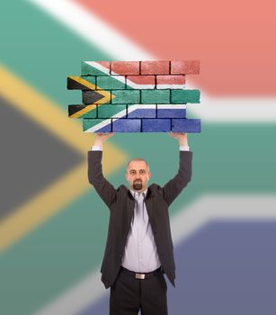 Businessman holding a large piece of a brick wall, flag of South Africa, isolated on national flag
