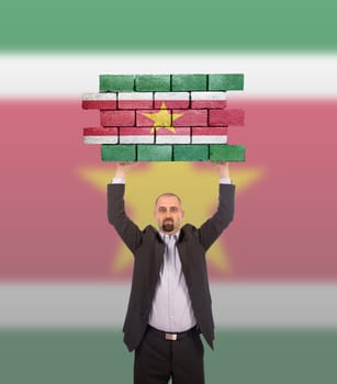 Businessman holding a large piece of a brick wall, flag of Suriname, isolated on national flag