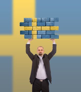 Businessman holding a large piece of a brick wall, flag of Sweden, isolated on national flag