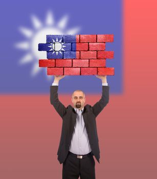 Businessman holding a large piece of a brick wall, flag of Taiwan, isolated on national flag