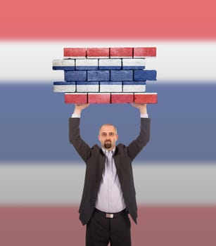 Businessman holding a large piece of a brick wall, flag of Thailand, isolated on national flag