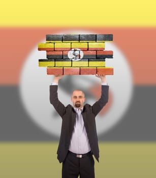 Businessman holding a large piece of a brick wall, flag of Uganda, isolated on national flag