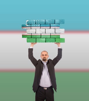 Businessman holding a large piece of a brick wall, flag of Uzbekistan, isolated on national flag