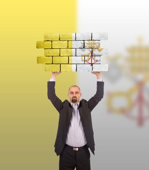 Businessman holding a large piece of a brick wall, flag of Vatican City, isolated on national flag