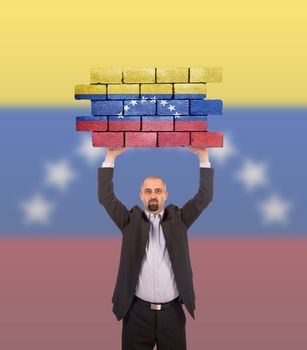Businessman holding a large piece of a brick wall, flag of Venezuela, isolated on national flag