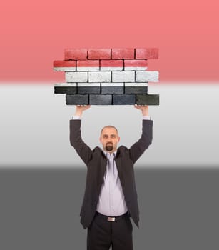 Businessman holding a large piece of a brick wall, flag of Yemen, isolated on national flag