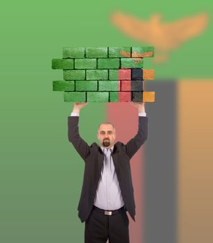 Businessman holding a large piece of a brick wall, flag of Zambia, isolated on national flag