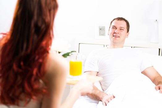 woman brought her boyfriend breakfast in bed, holding a tray of juice and breakfast