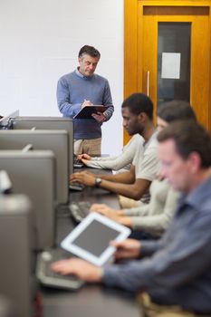 Teacher writing on clipboard during class in computer room in college