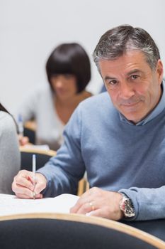 Man looking up from taking notes and smiling in a lecture in college