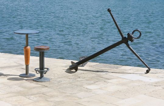 old anchor and empty chair and table near the sea in late summer