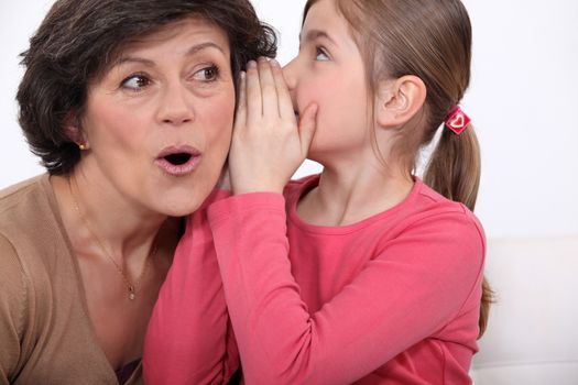 Girl whispering a secret to her grandmother