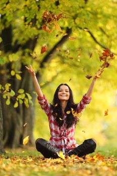 woman drop up leaves in autumn park