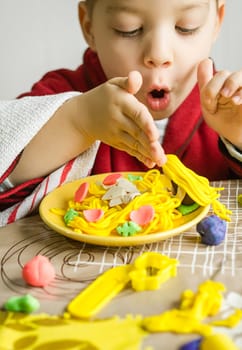 Cute child playing with his original spaghetti dish, made with colorful plasticine