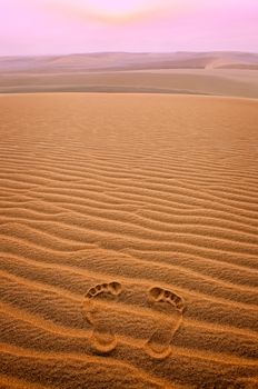 Two footprints in sand in the desert at sunset