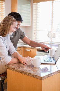 Man pointing at laptop screen by woman in the kitchen