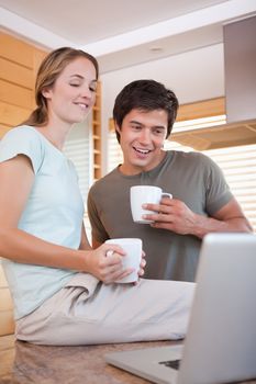 Young couple using laptop while drinking coffee in the kitchen