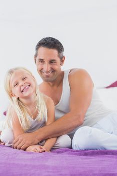 Smiling father and his daughter sitting on a bed in the bedroom