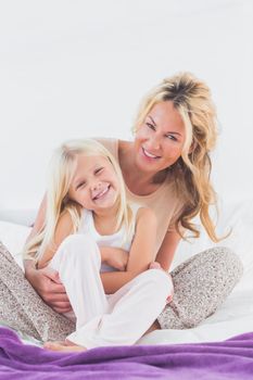 Mother and her daughter looking at camera sitting on bed