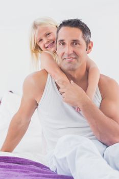 Smiling father and his daughter doing piggyback on a bed in the bedroom