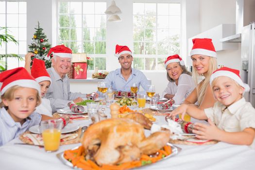 Smiling family around the dinner table at christmas wearing santa hats