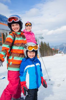 Two happy smiling kids in ski goggles and a helmet with his mother in the mountains