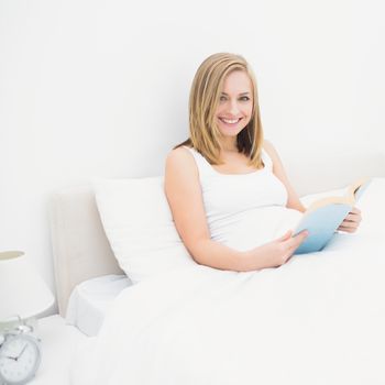 Portrait of happy young woman reading book in bed at home