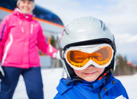 Portrait closeup of happy smiling boy in ski goggles and a helmet with his mother