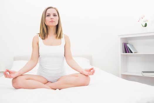 Young woman sitting in lotus position on bed at home