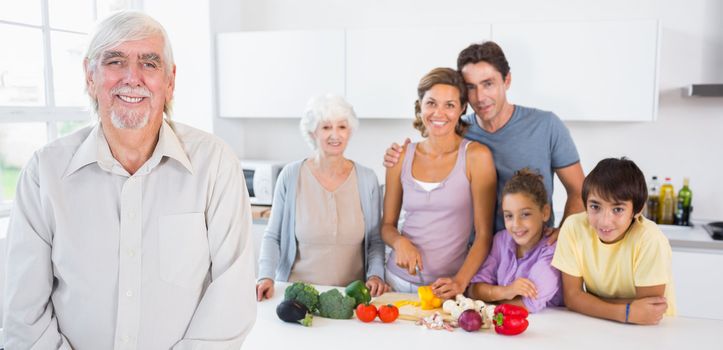 Grandfather standing by kitchen counter with family behind him 