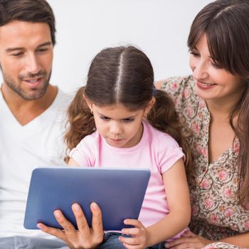 Smiling parents watching young daughter using tablet pc on couch