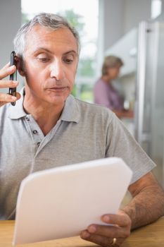 Focused mature man calling with a sheet of paper in the kitchen