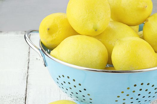 Retro light blue colander filled with fresh lemons over a rustic background.
