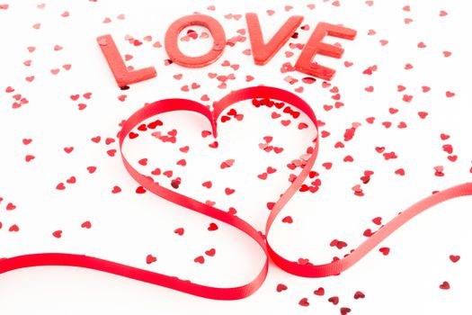 Heart shaped ribbon with confetti and word love on white background