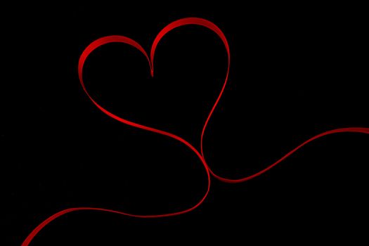 Red ribbon in heart shape on black background