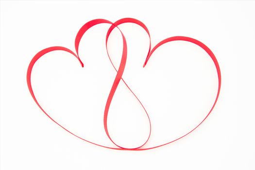Pink ribbon shaped into intertwining hearts on white background