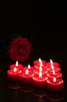 Romantic candles with red rose on black background
