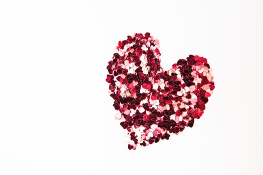 Pink and red confetti in heart shape on white background
