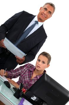 Smiling businessman standing over his overworked assistant