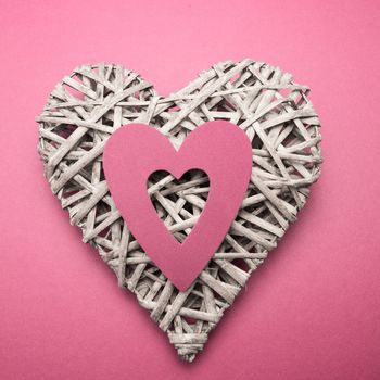 Wicker heart ornament with pink paper cut out on pink background