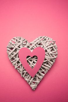 Wicker heart ornament with pink paper cut out on pink background