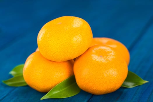 Pile of mandarins with leaves on blue wood (Selective Focus, Focus on the front of the mandarin on top and on the right) 